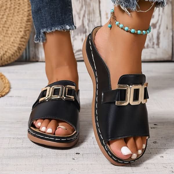 Close-up of black slip-on wedge sandal with metallic buckle detail worn on foot