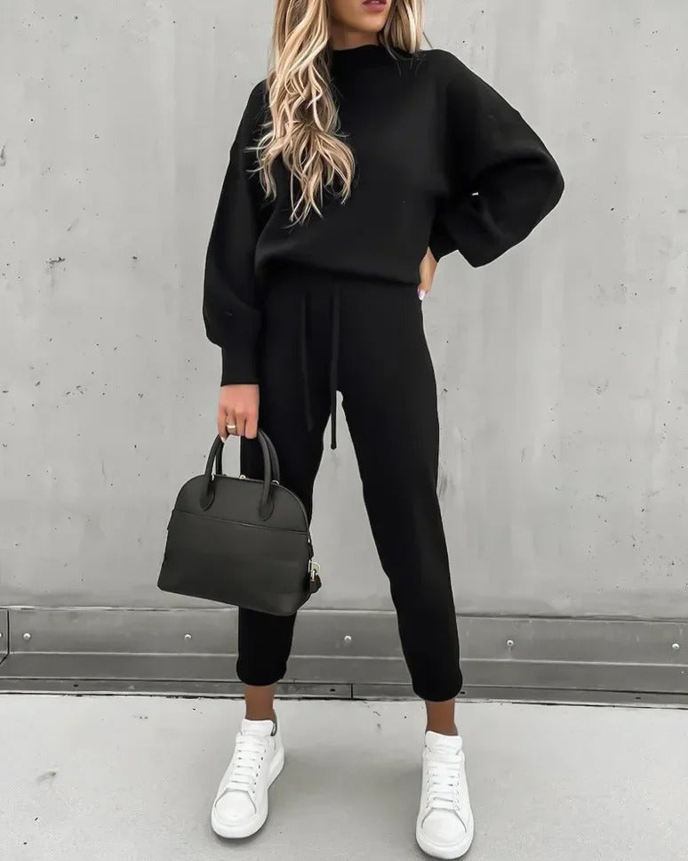Woman wearing a black lounge suit holding a black handbag and white sneakers