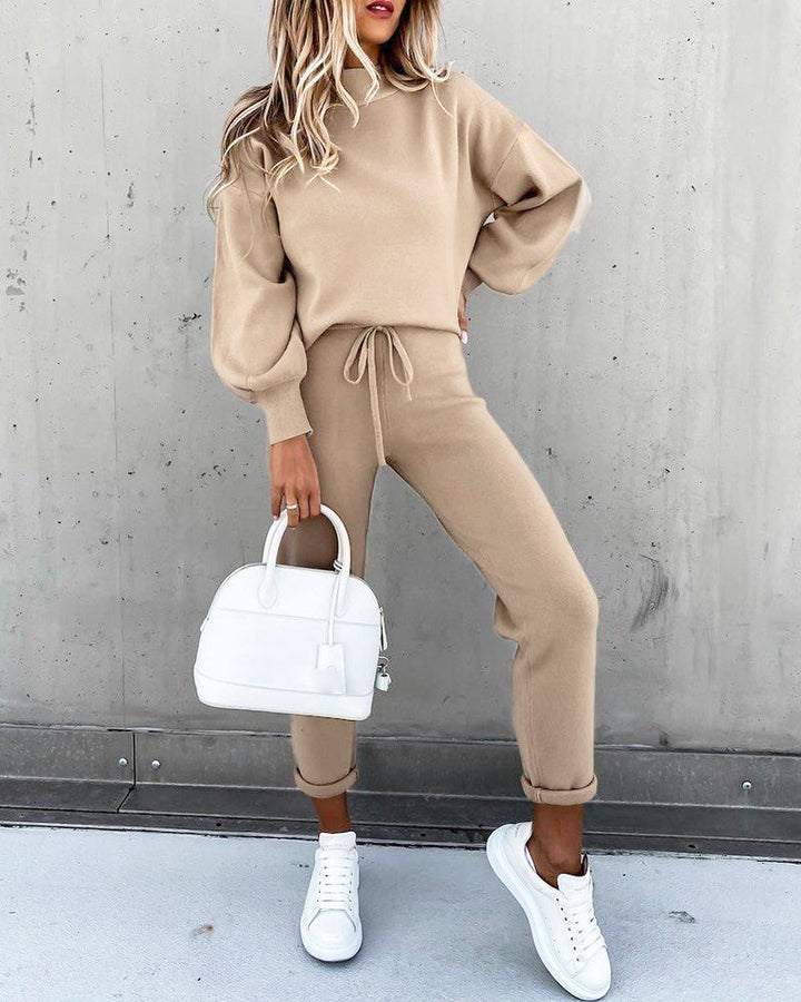 Woman wearing a khaki lounge suit holding a white handbag and white sneakers