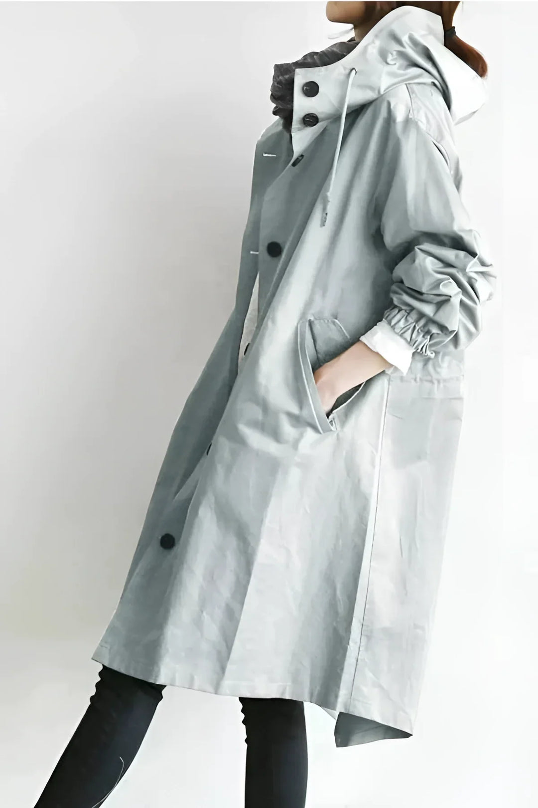 Side profile of a woman in a light gray hooded raincoat with pockets
