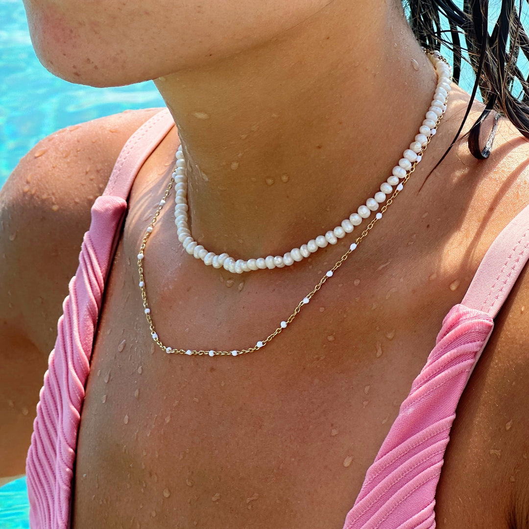 A woman wearing the white enamel bead choker layered with another necklace near a pool.