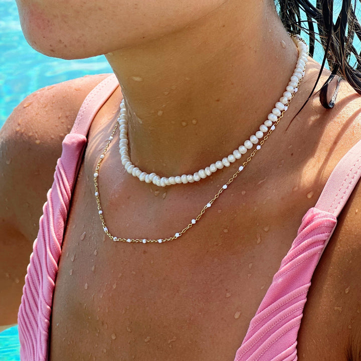 A woman wearing the white enamel bead choker layered with another necklace near a pool.