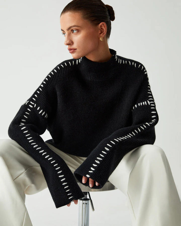Woman wearing a black oversized mock neck pullover sweater seated