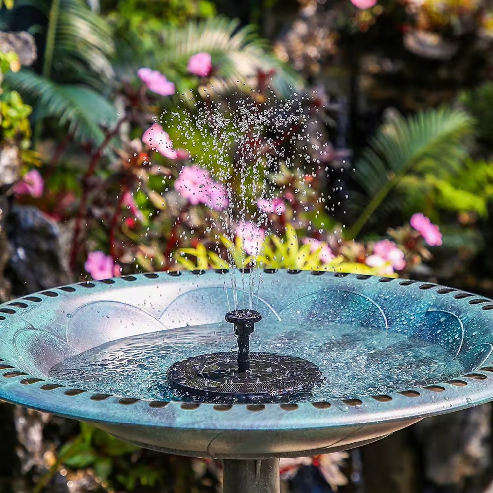 Solar powered bird bath fountain operating in a decorative bowl with pink flowers in the background