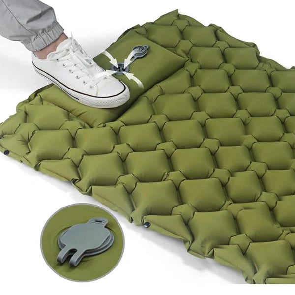 Foot pressing down on the inflation valve of a green camping mattress