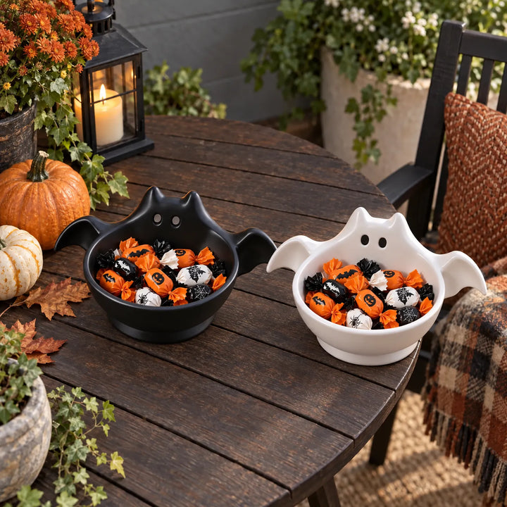 Black and white bat-shaped Halloween candy bowls displayed side by side on a rustic wooden table
