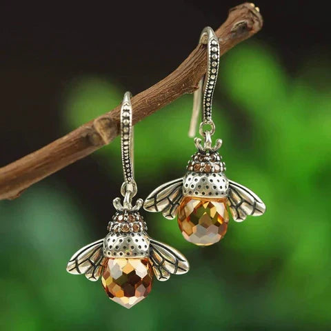 Close-up of queen bee silver crystal drop earrings resting on a branch