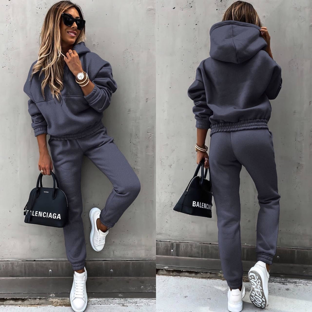 Woman wearing a dark grey casual lounge set and white sneakers against a concrete wall