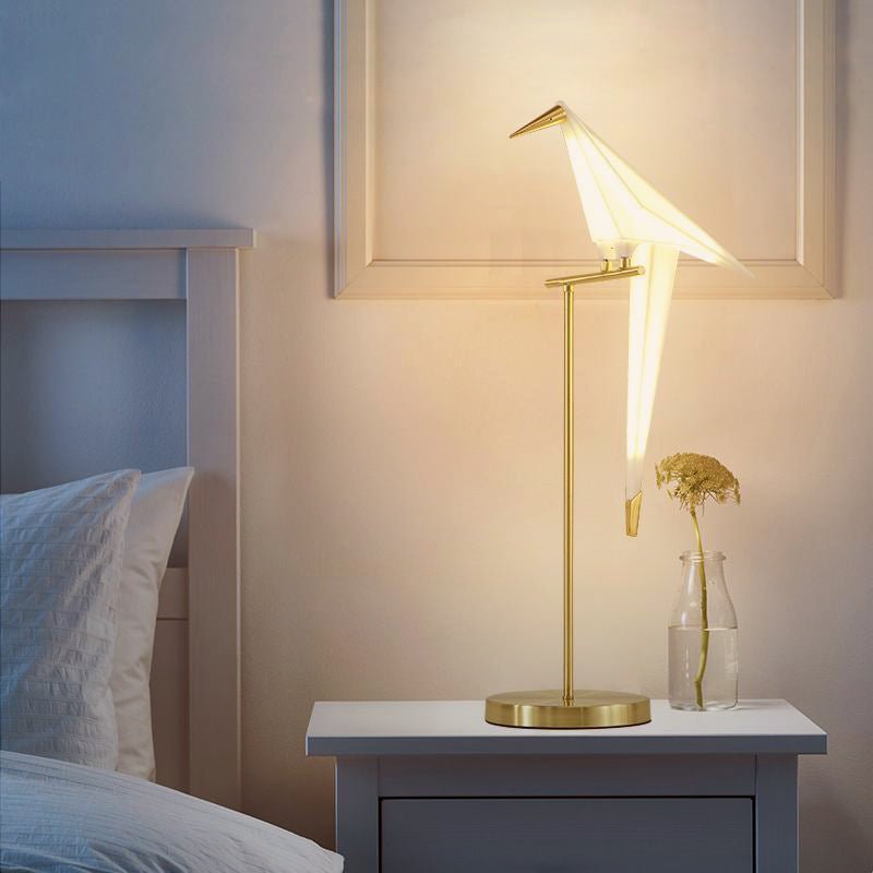 Magnetic origami bird table lamp casting warm light on a bedside table