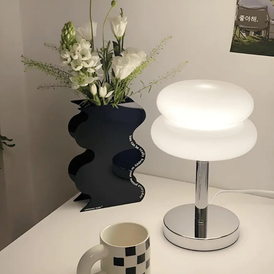 Macaron glass table lamp in white emitting a soft warm glow on a white desk