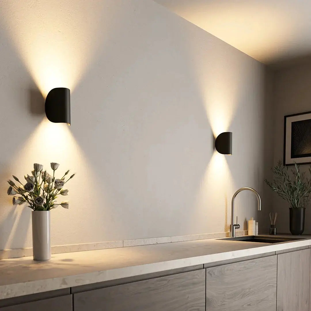 Modern black LED wall lamp mounted on a wall casting warm light in a kitchen setting