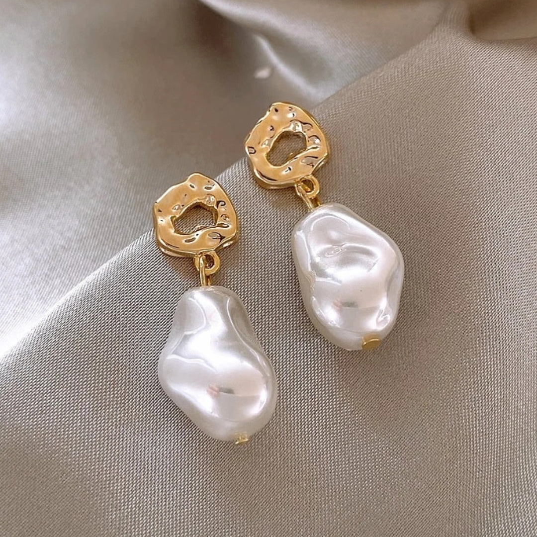 Women's gold boho pearl drop earrings resting on a silk background