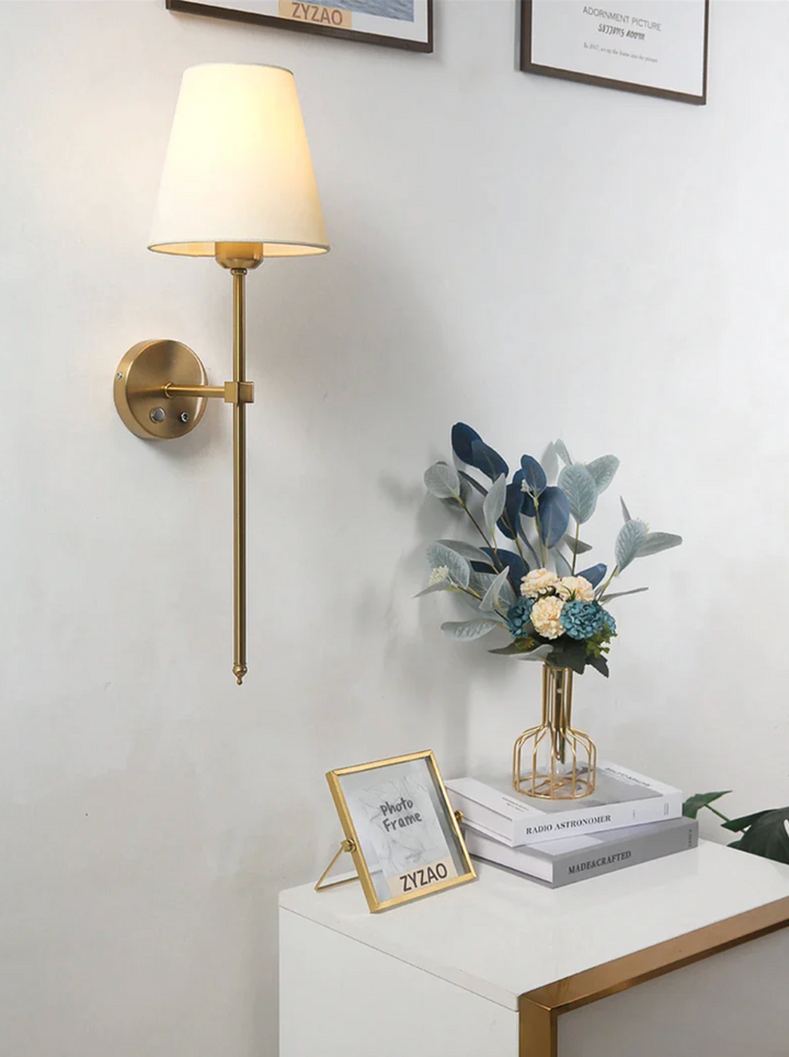 A single gold wireless wall lamp mounted above a modern white bedside table with decor