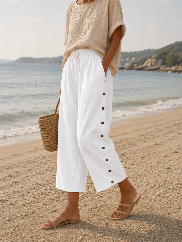 Woman wearing white casual capri pants with button detail on a beach