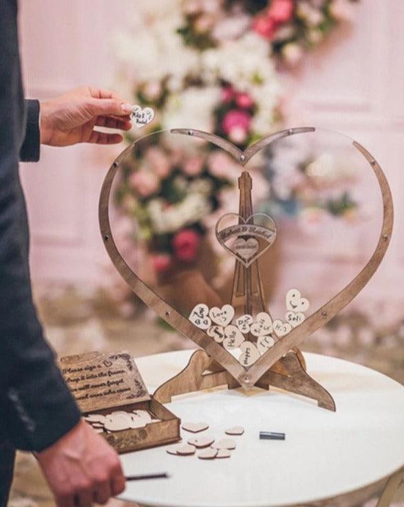 Guest holding a small wooden heart next to the heart-shaped guest book frame on a table