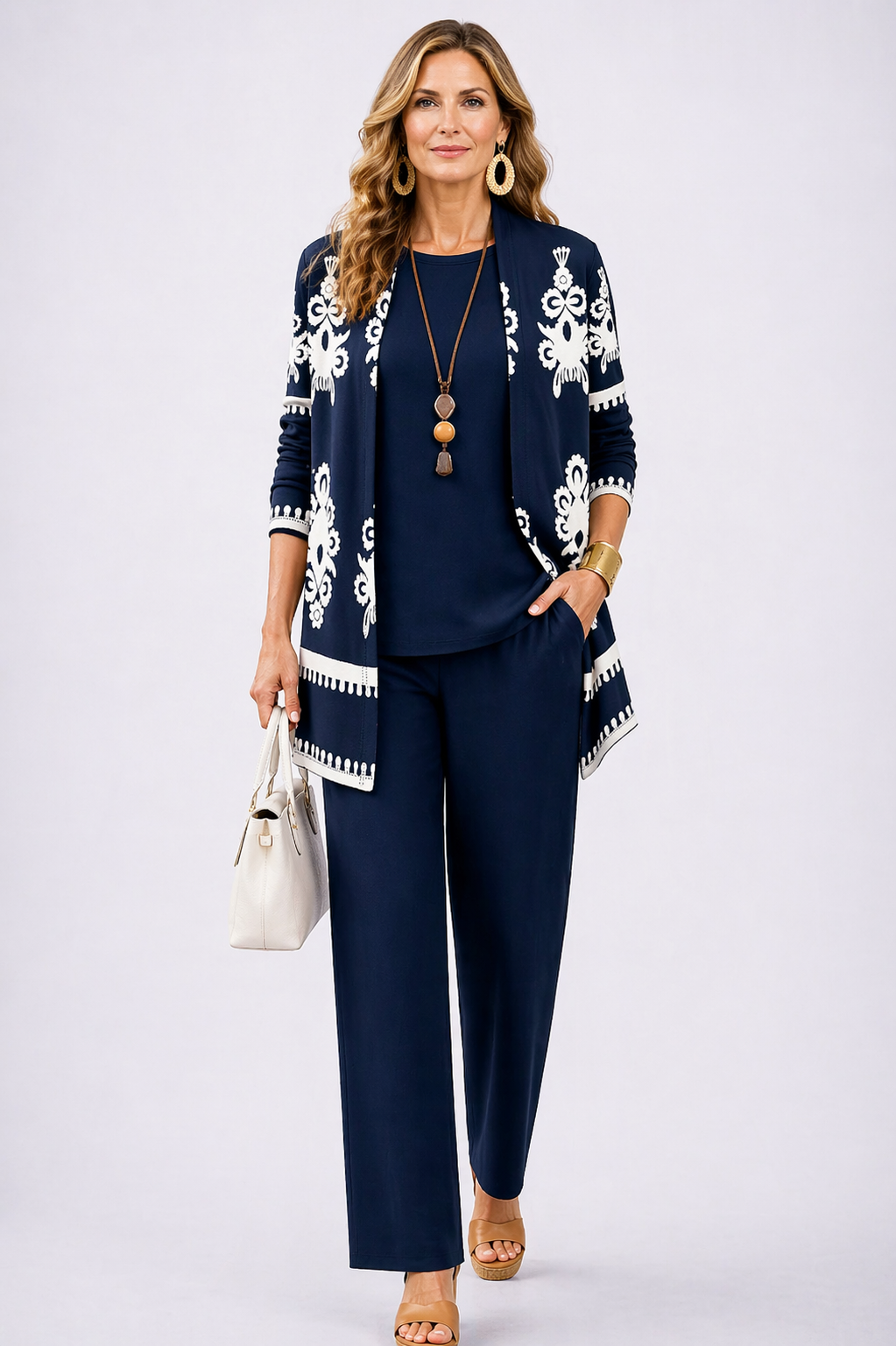 Model wearing a navy blue three-piece cardigan, top, and wide-leg trouser set with a white handbag.