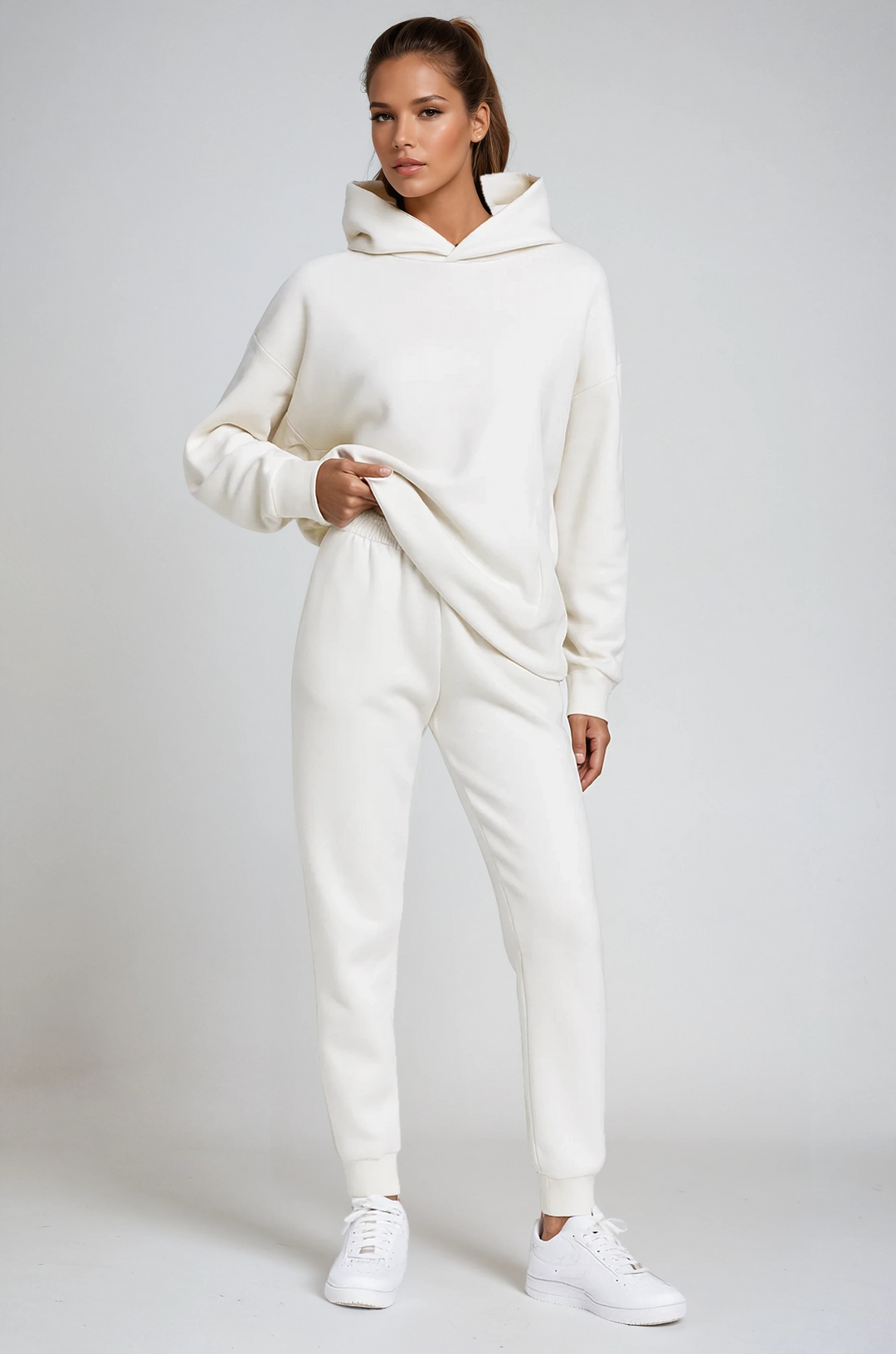 Model standing wearing a white hooded jogging set with white sneakers