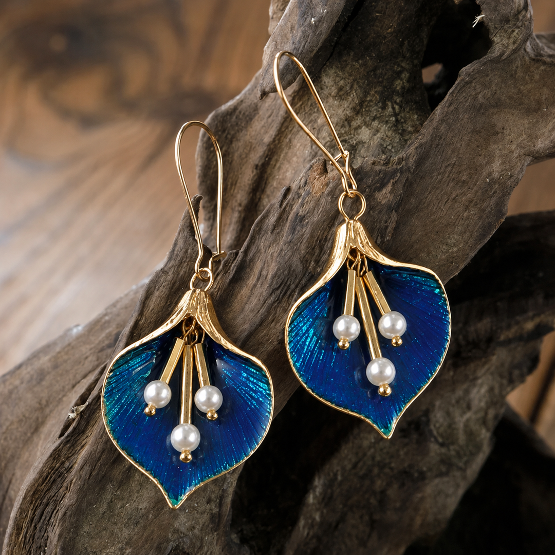 Women's blue lotus dangle earrings with gold finish and pearl accents displayed on textured wood