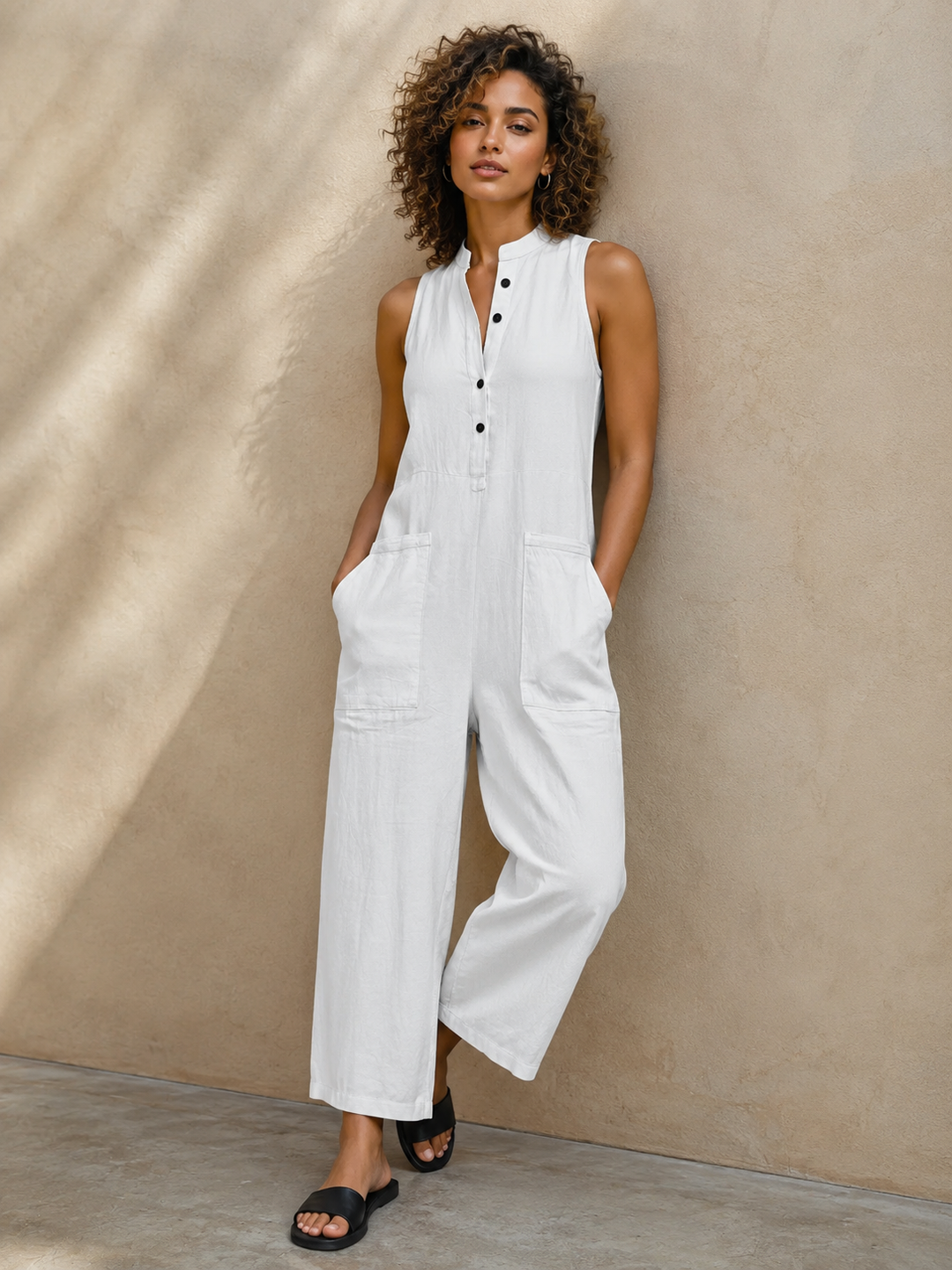 Woman wearing a white sleeveless wide leg jumpsuit leaning against a textured wall