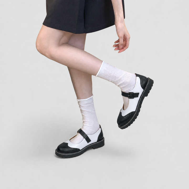 Side view of woman wearing black and white Mary Jane shoes with white socks and skirt