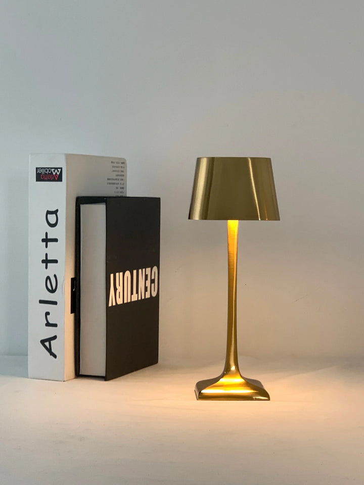 Elegant gold cordless LED table lamp glowing beside books