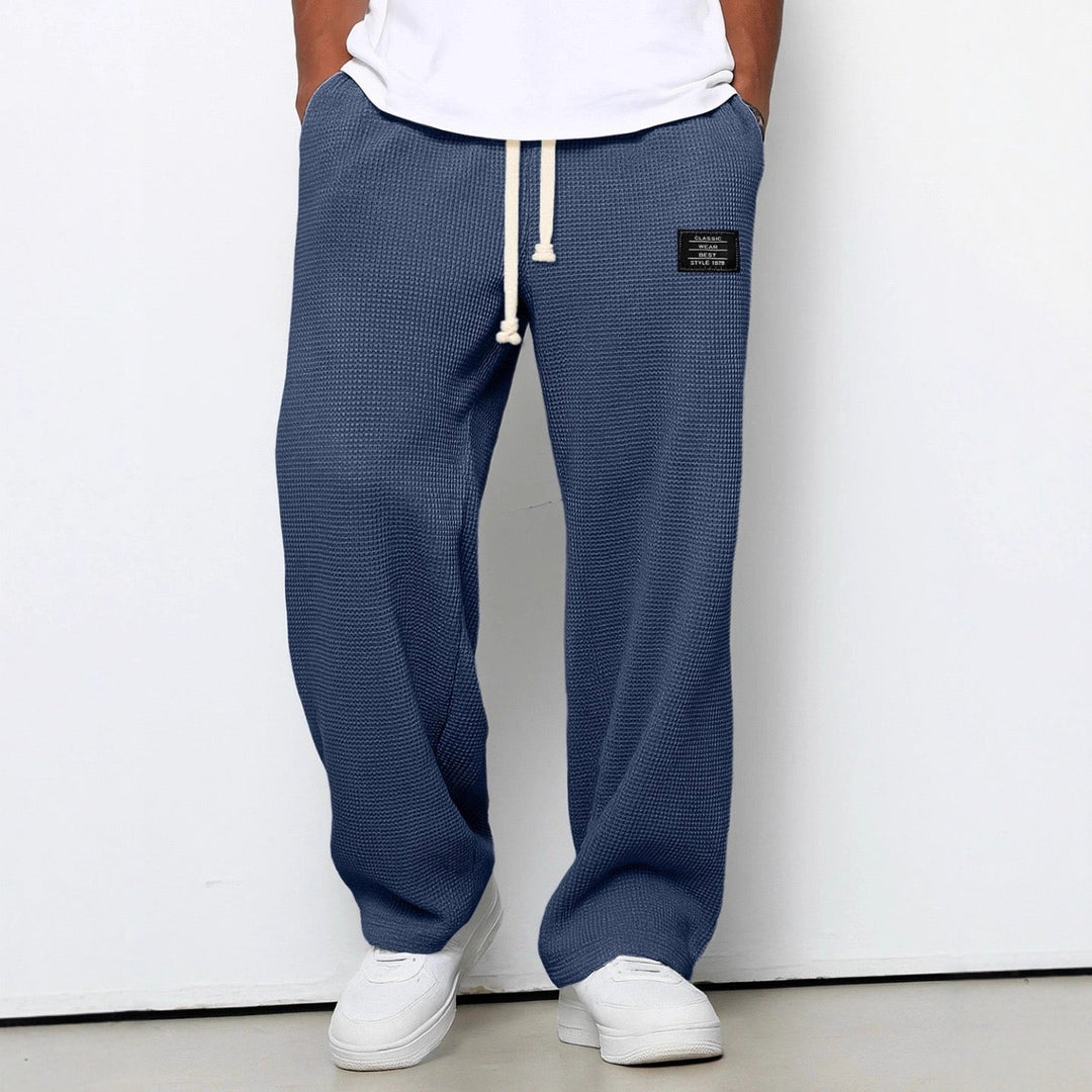 Man wearing blue relaxed fit trousers with drawstring and white sneakers