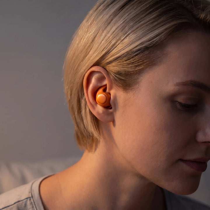 Close-up of a person wearing an orange wireless sleep earbud comfortably in bed