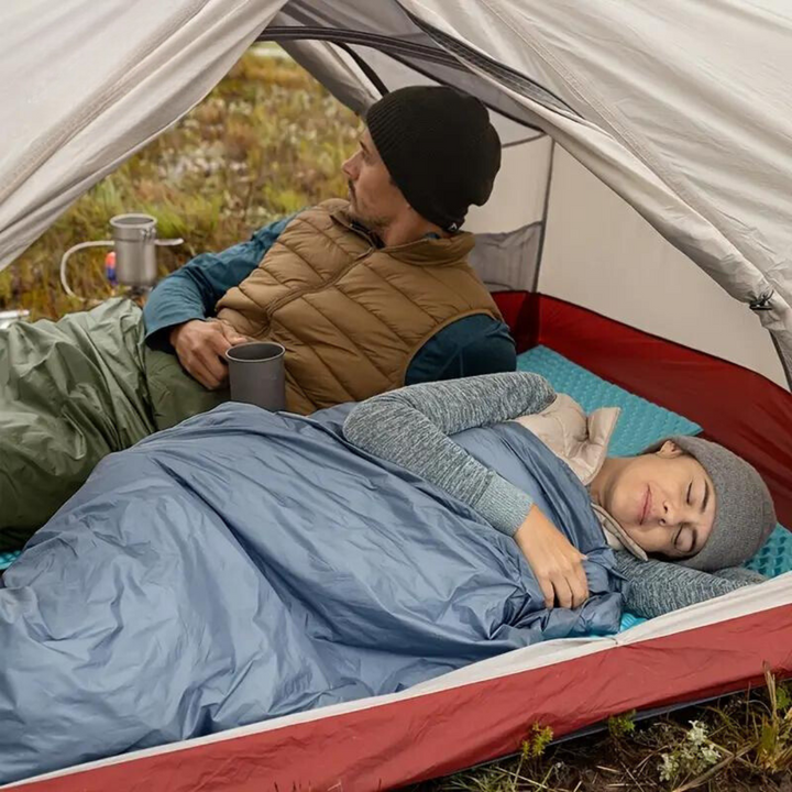 Couple camping inside a tent using a blue sleeping bag