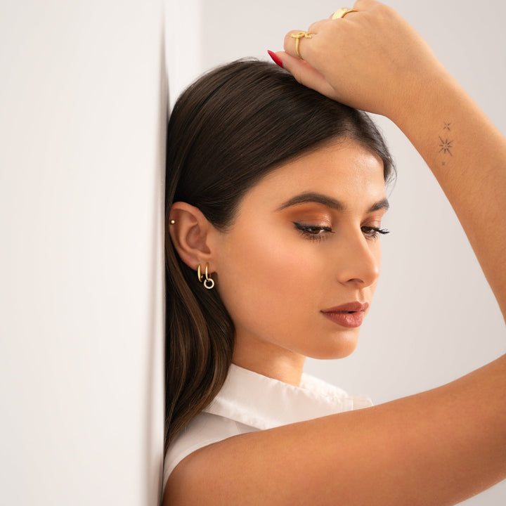 Model posing with a hand to her head, showcasing the gold linked hoop earrings