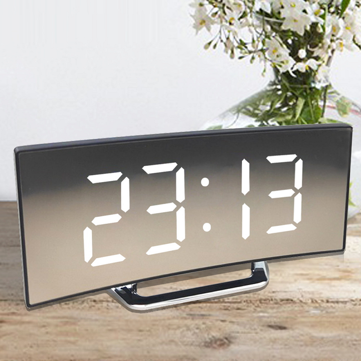 Curved digital LED alarm clock with white digits and mirrored surface on wooden table