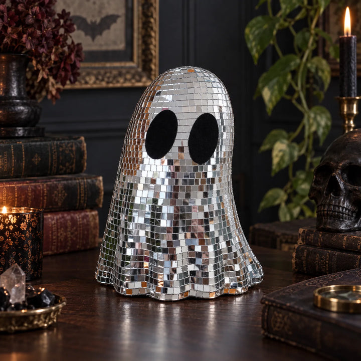 Disco ghost ornament styled on a dark wooden table with candles and vintage books