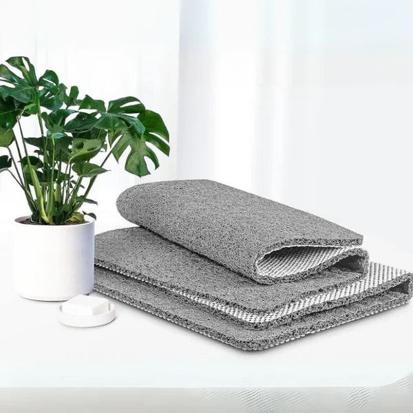 Folded grey shower mat displayed with a potted plant on a white surface