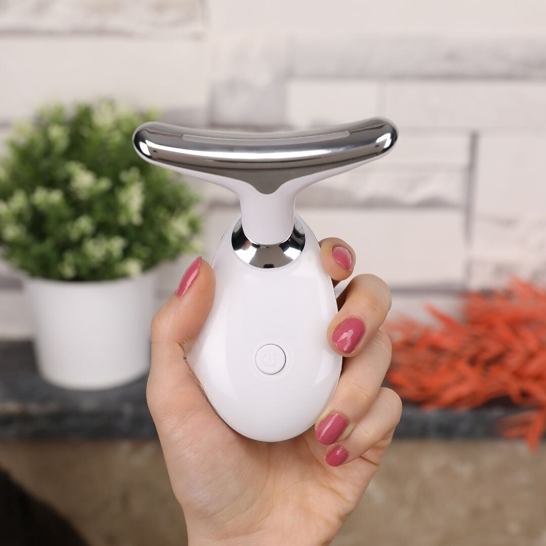 Close-up of a hand holding the white and silver 3-in-1 face and neck massager