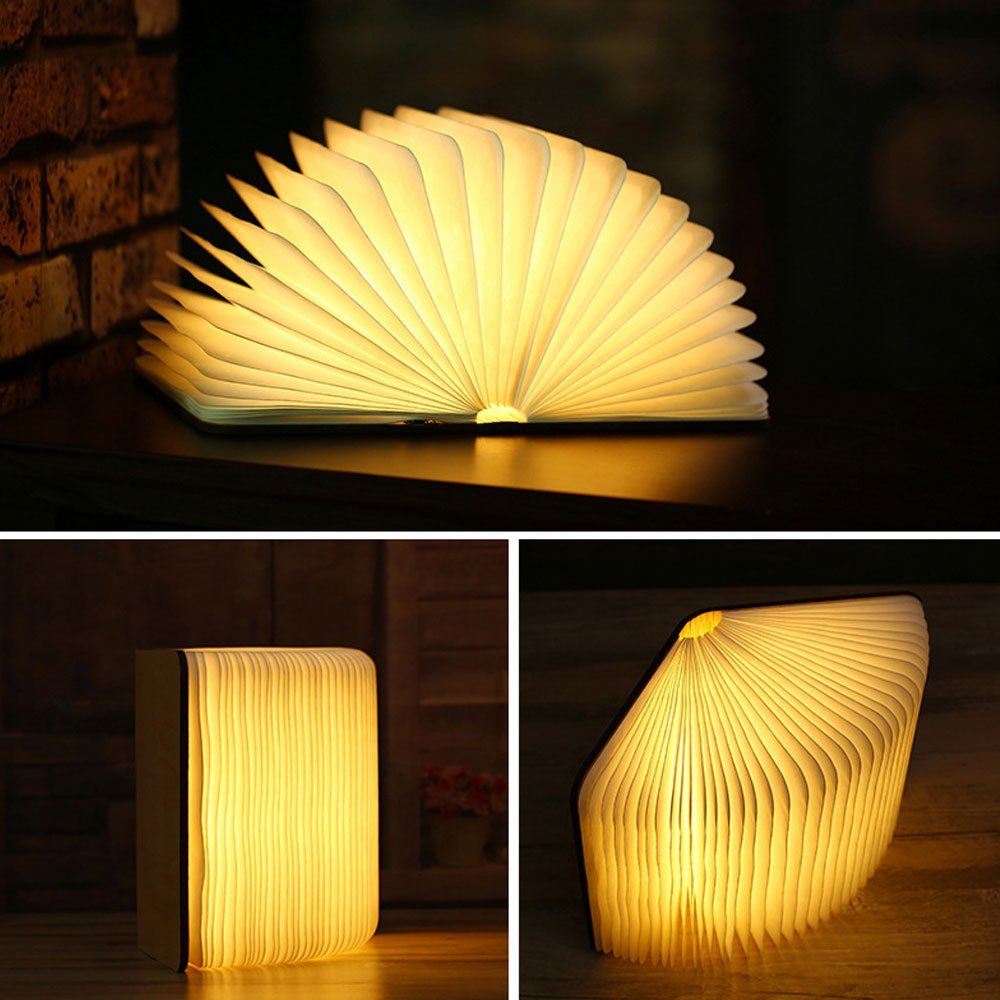 Folding LED book lamp opened wide on a dark wooden surface with a warm glow