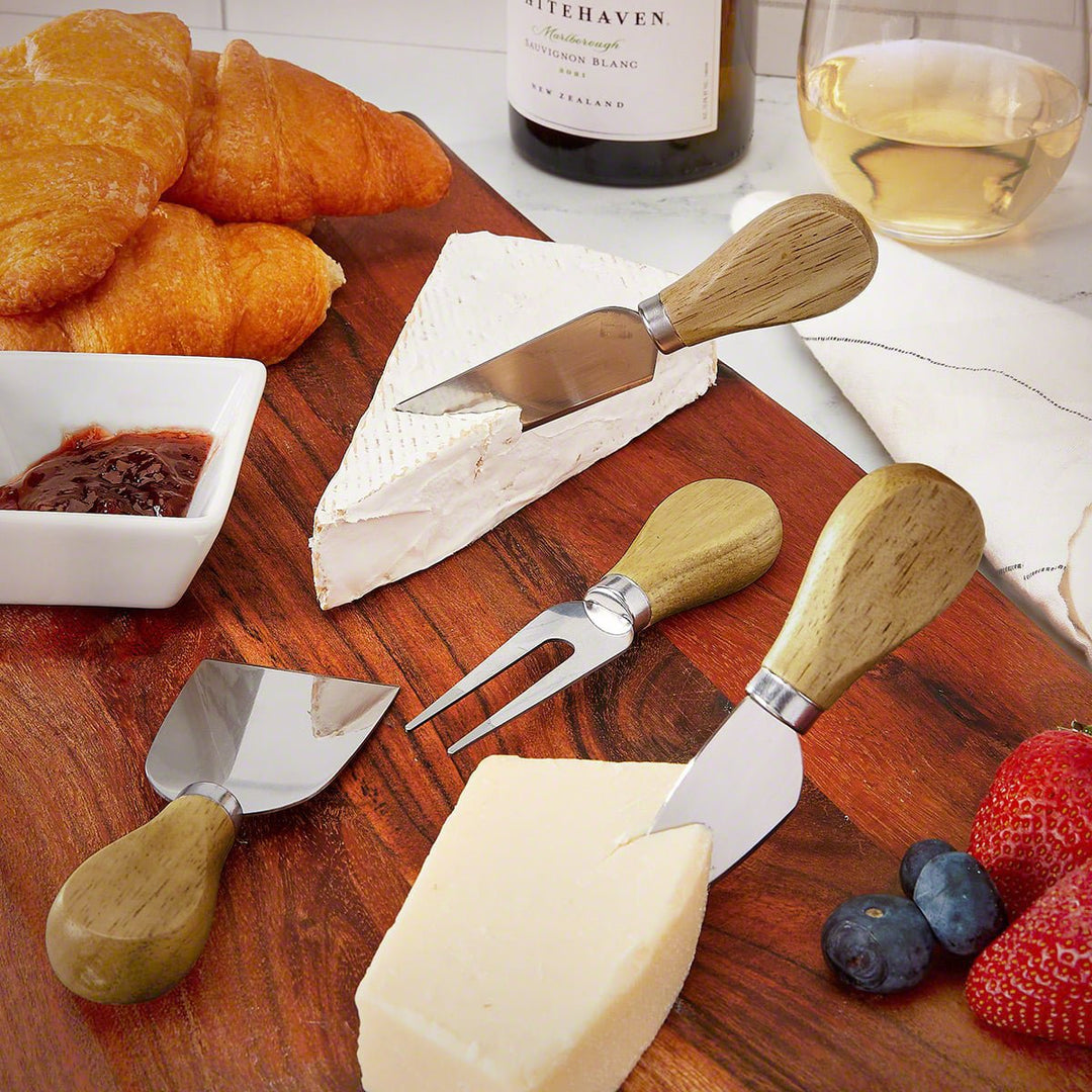 Four-piece cheese knife set with wooden handles displayed on a charcuterie board with cheese and fruit