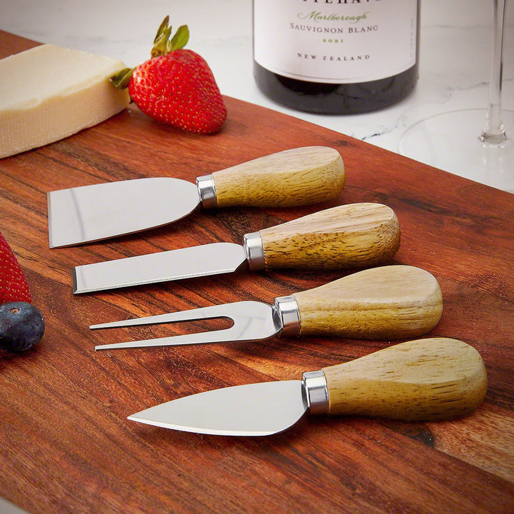 Four cheese knives arranged neatly on a wooden serving board next to wine and strawberries