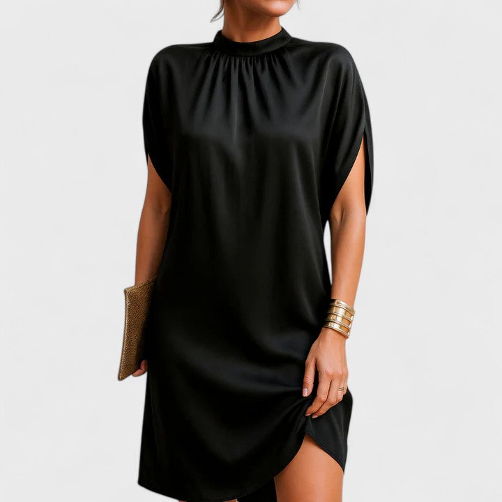 Woman wearing a black mock neck dress with split batwing sleeves holding a clutch