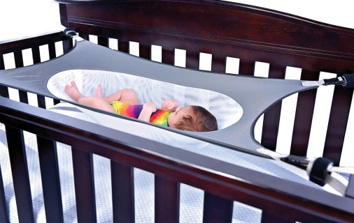 Grey baby sleep aid hammock securely attached inside a wooden cot for nursery