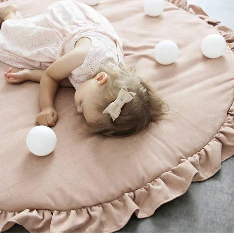 Close-up of a baby resting peacefully on a plush round nursery crawling mat surrounded by white decorative balls.