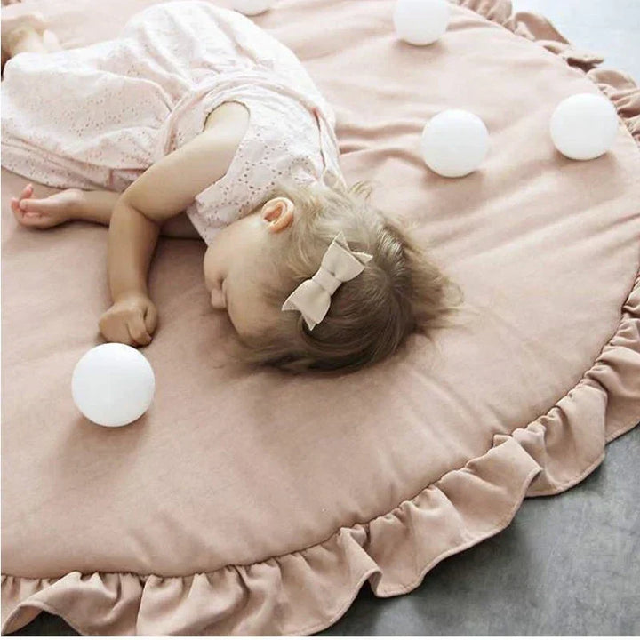 Close-up of a baby resting peacefully on a plush round nursery crawling mat surrounded by white decorative balls.