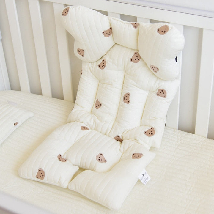 Plush baby stroller cushion with bear pattern displayed flat on a white crib