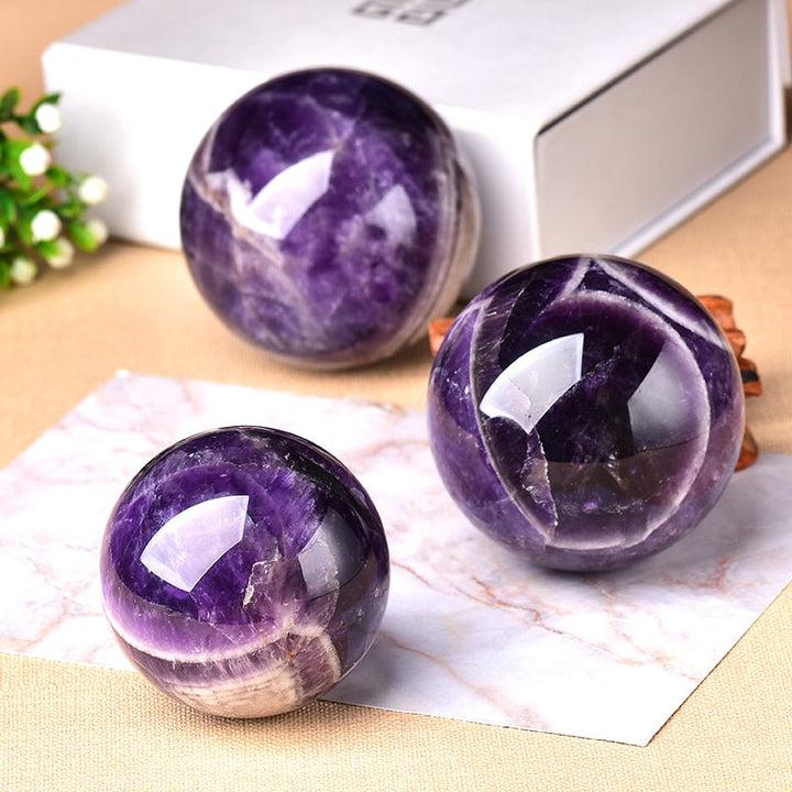 Three different sized polished amethyst spheres arranged together on a surface
