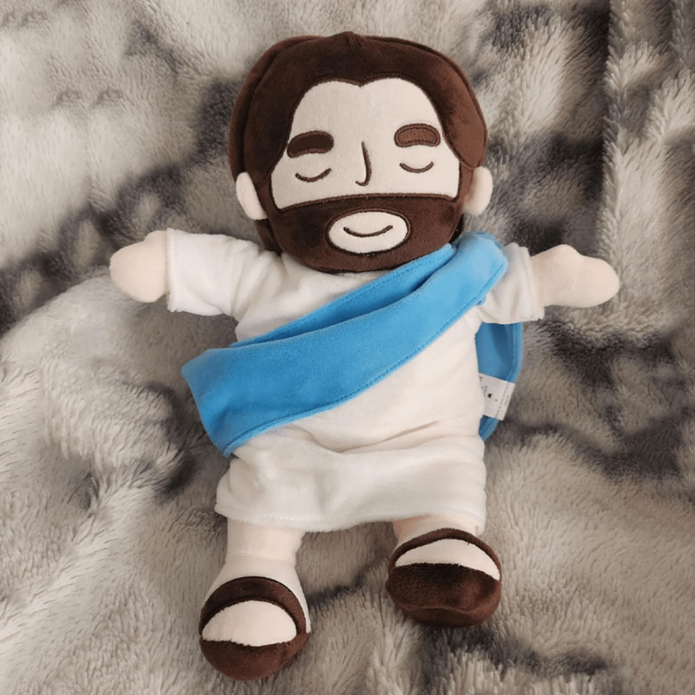 Blue sash variant of the Jesus sleep aid plush resting on a blanket