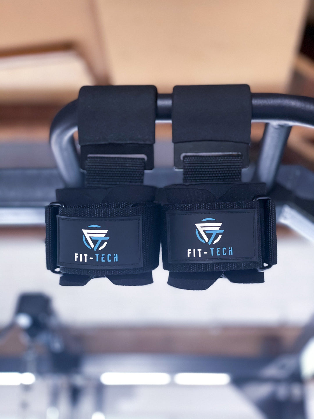 Pair of black lifting hooks hanging from a pull-up bar in a gym
