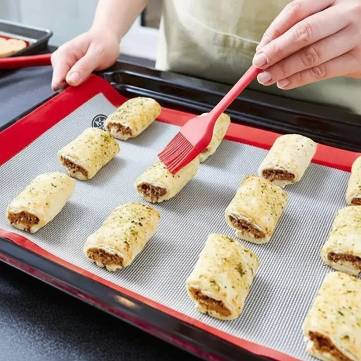 Close-up of a red silicone brush applying glaze to baked pastries