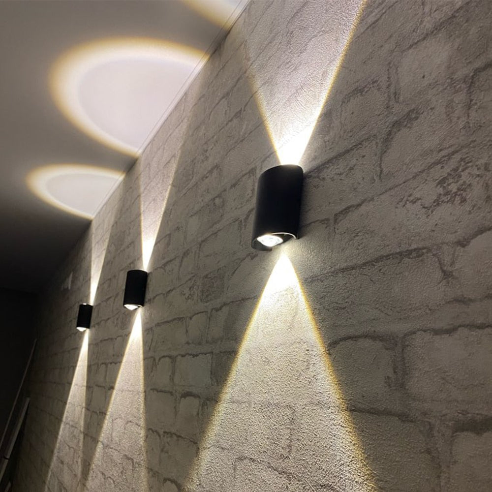 Multiple black LED wall lamps installed along a textured brick hallway emitting warm light patterns