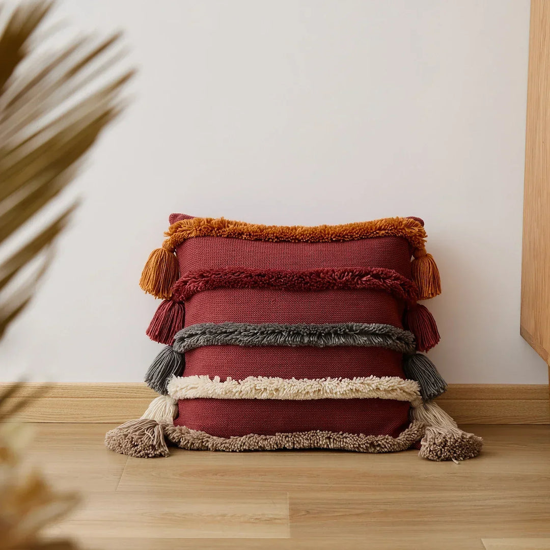 Red variant of the fringed striped cushion cover resting against a white wall