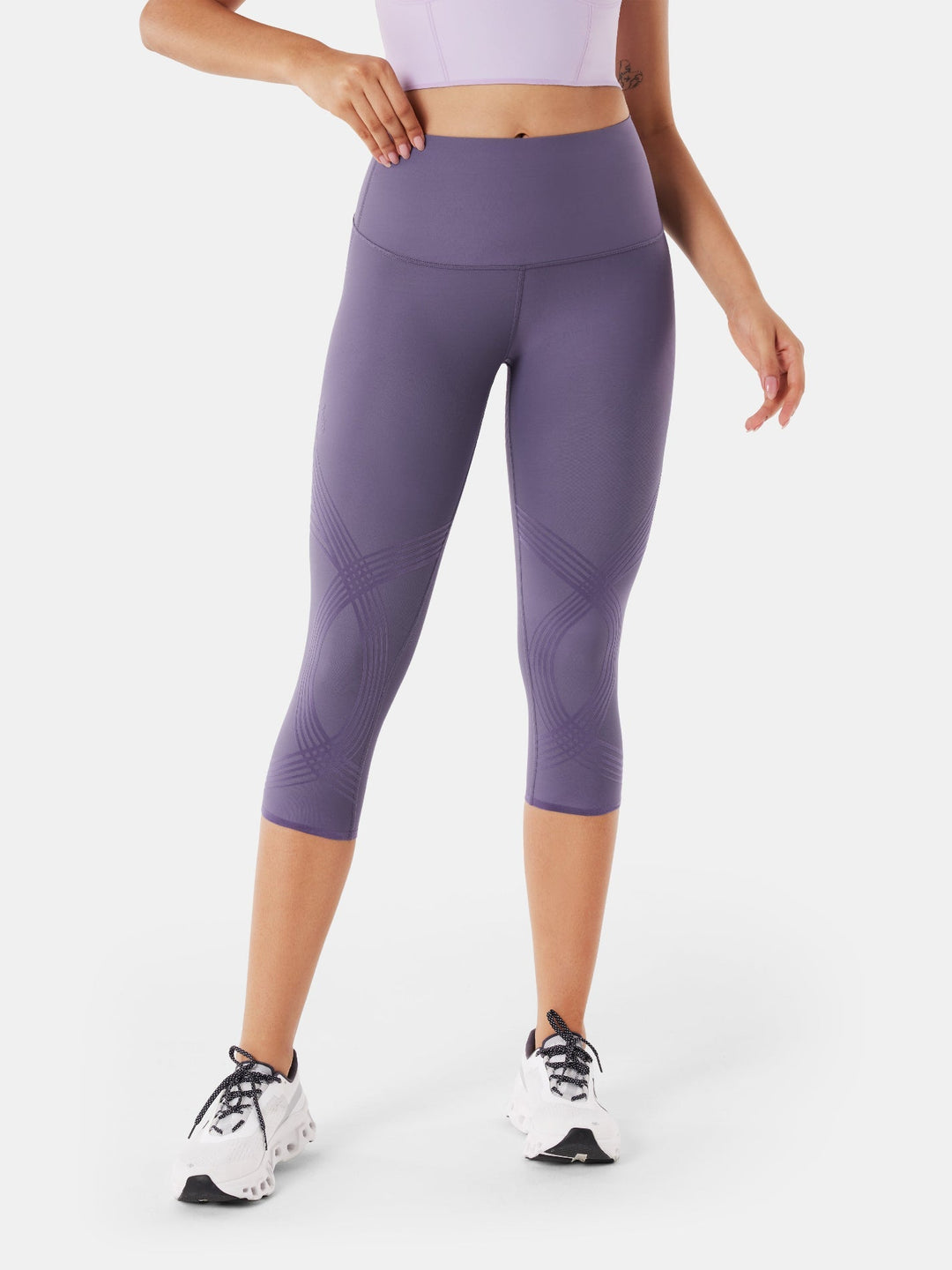 Model wearing purple high compression capri leggings standing with white sneakers