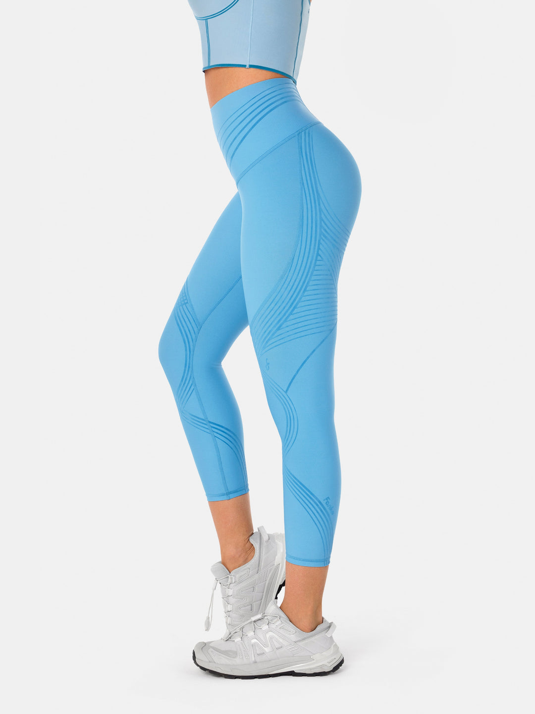 Side profile view of a woman wearing light blue high-rise 7/8 gym leggings with subtle athletic contour lines.
