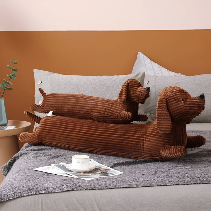 Brown dachshund plush pillow placed on a grey bedspread next to a coffee cup